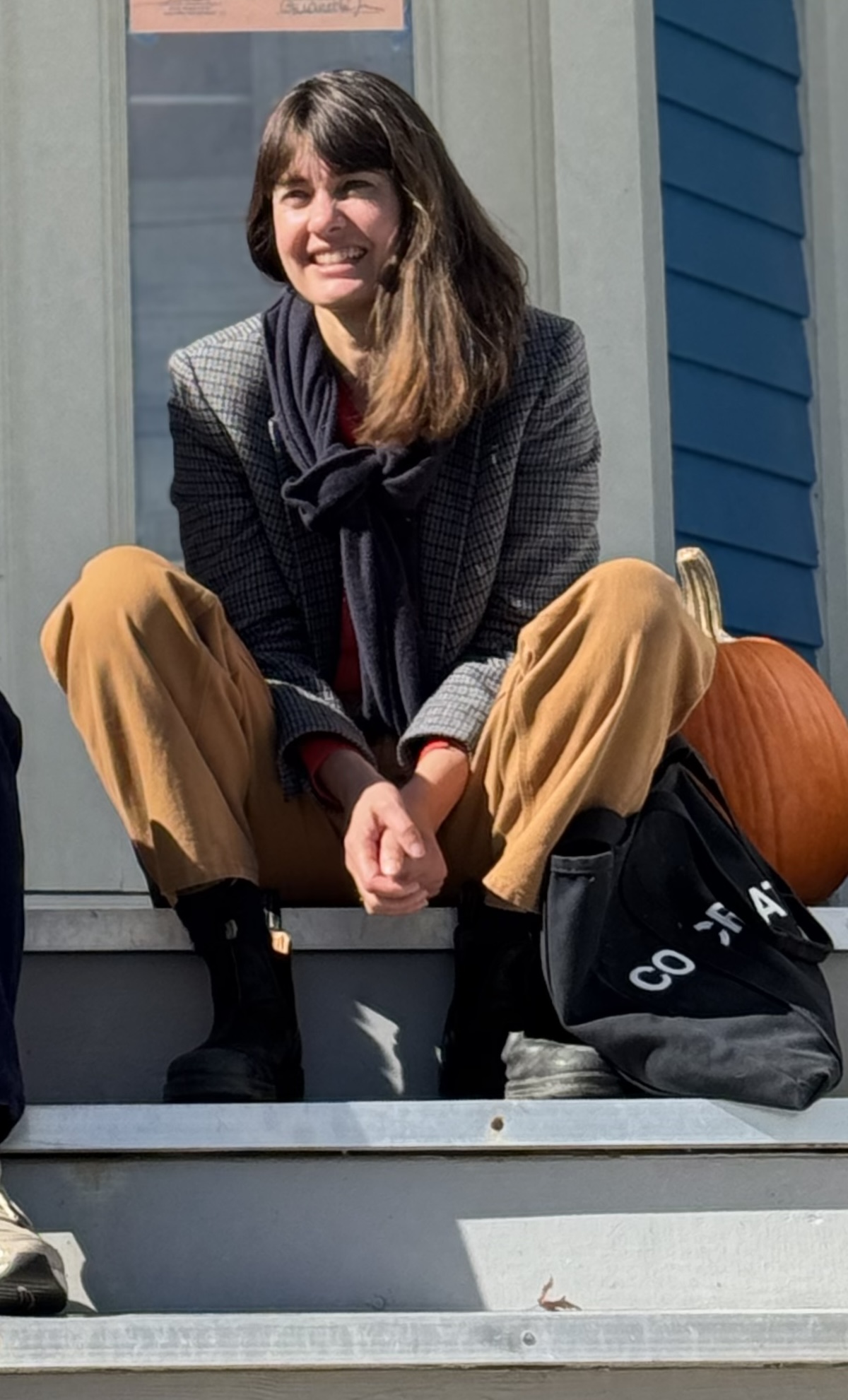 Smiling woman with a pumpkin sitting on sunlit porch steps