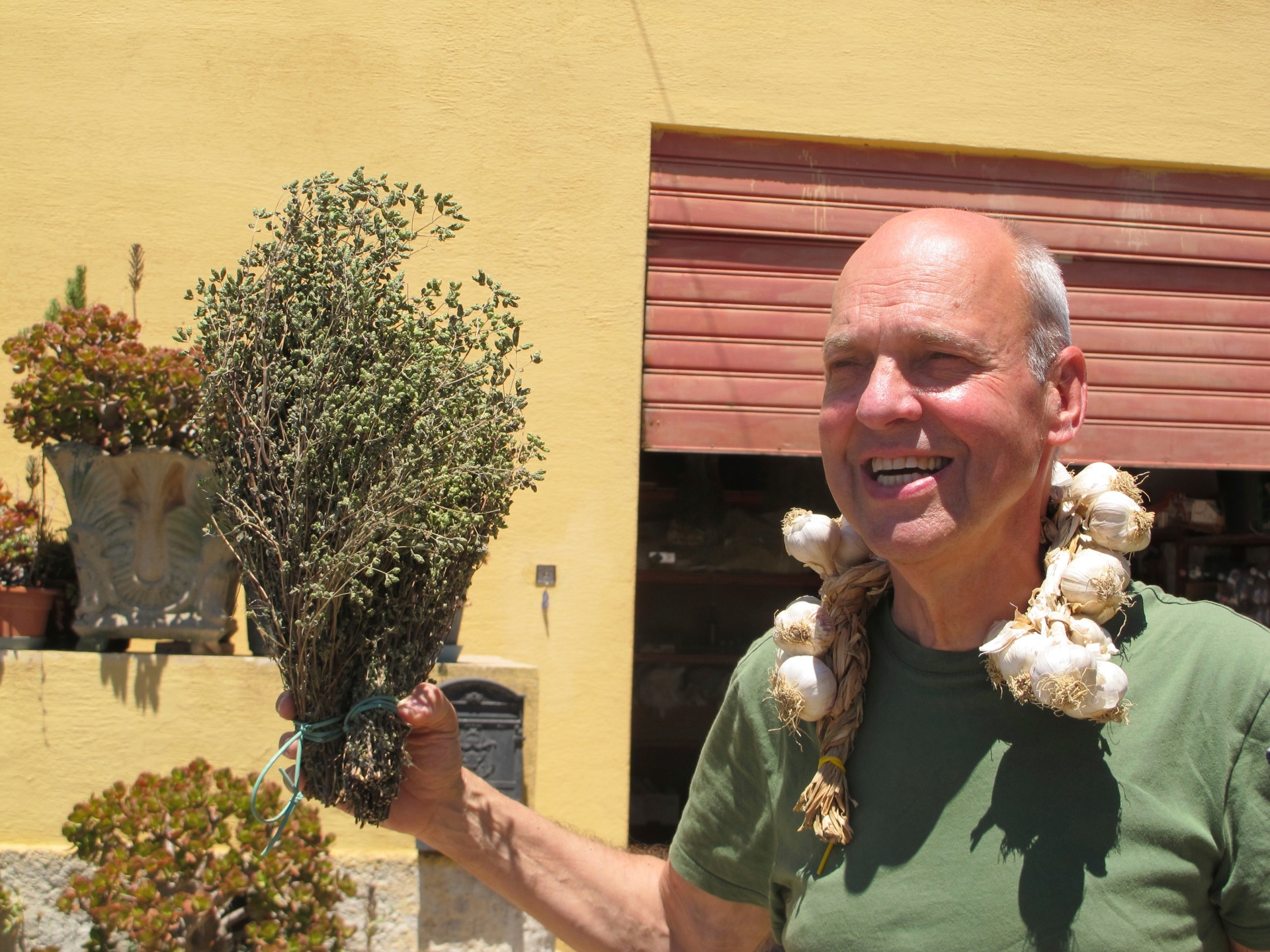 Smiling man holding a bundle of dried oregano with a braid of garlic draped over his shoulder